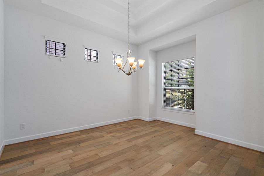 Spacious room featuring wood-finish flooring, white baseboards, and a tray ceiling with a chandelier