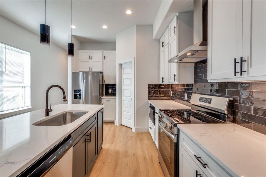 Kitchen with white cabinetry, wall chimney range hood, sink, and appliances with stainless steel finishes
