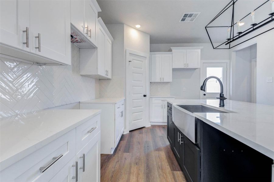 This gourmet kitchen is as beautiful as it is practical showcasing abundant cabinetry, gleaming white quartz counters, soft-close drawers, and a classic herringbone tile backsplash. Every inch is designed for everyday elegance and modern efficiency.