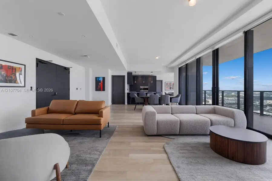 Open-concept living space featuring wood-finish flooring, floor-to-ceiling glass wall, recessed lighting, and kitchen cabinetry with integrated appliances