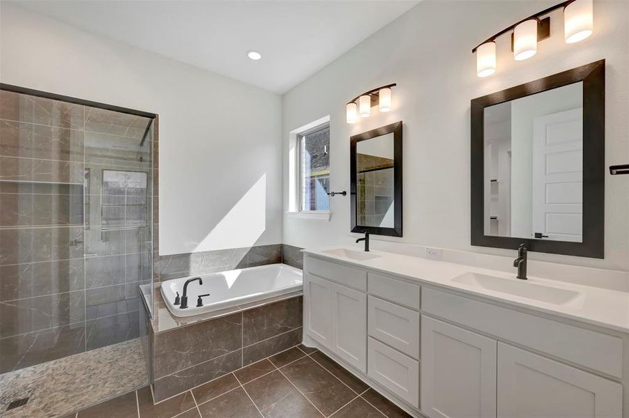 Full bath with double vanity, a stall shower, a bath, and dark tile patterned floors