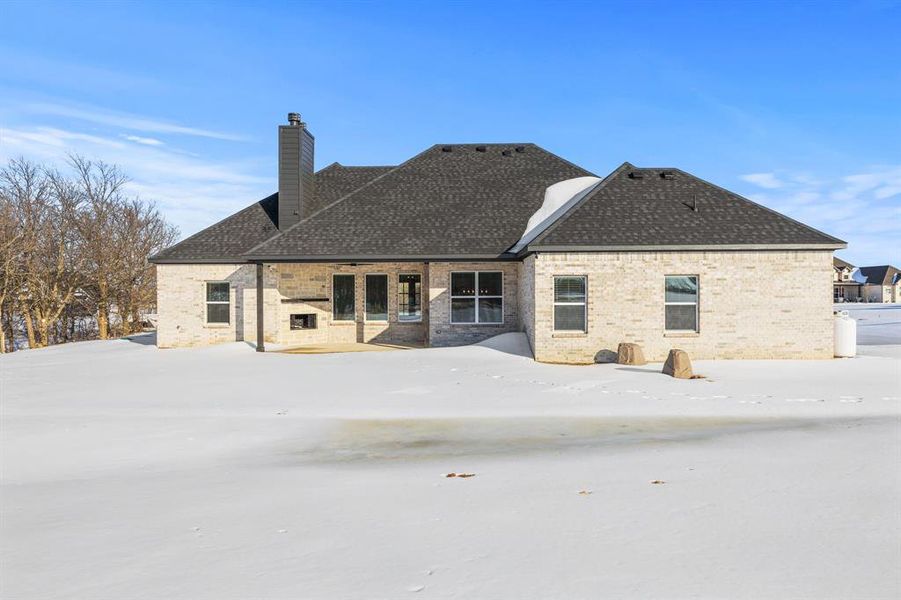 Snow covered house with a patio, brick siding, and a chimney