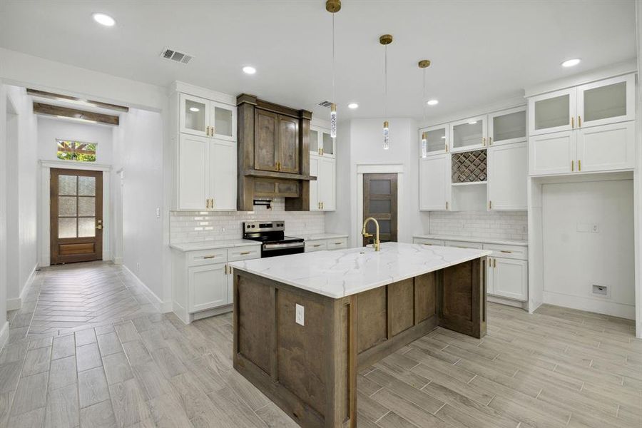 Kitchen with a center island with sink, white cabinetry, light stone countertops, and electric stove