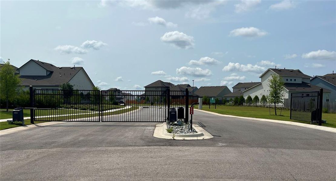 View of asphalt road with a gated entry, a gate, sidewalks, a residential view, and curbs
