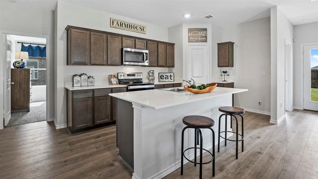 Kitchen featuring a central island with an undermount sink, white countertops, dark wood-finish cabinetry, stainless steel appliances, and wood-finish flooring