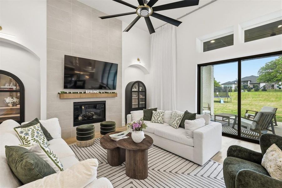 Living room with a tiled fireplace, a high ceiling, wood finished floors, and ceiling fan