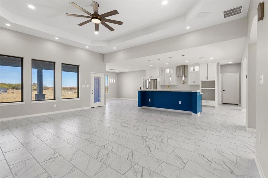 Unfurnished living room featuring light marble finish flooring, a raised ceiling, a ceiling fan, and recessed lighting