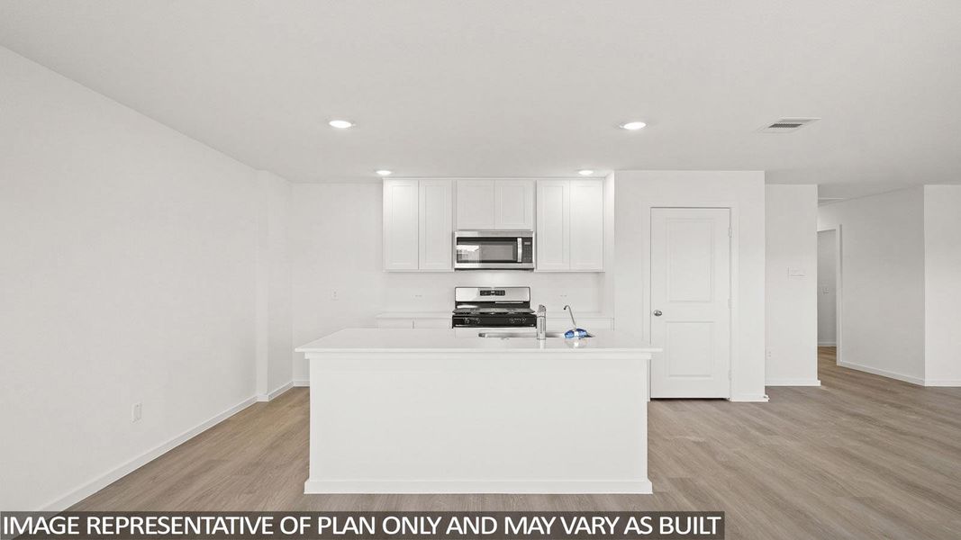 Kitchen with white cabinets, stove, a kitchen island with sink, stainless steel microwave, and light wood-type flooring