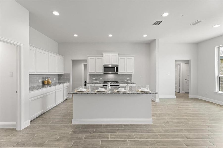 Kitchen featuring stainless steel microwave, range, a center island with sink, visible vents, and light stone countertops