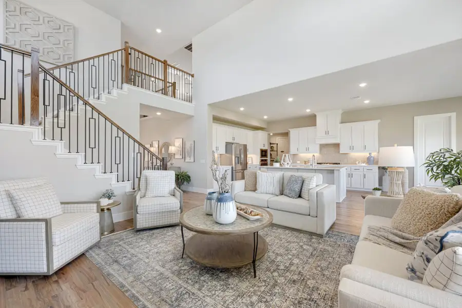 Open-concept living room with two-story staircase, hardwood floors, and white kitchen visible in background