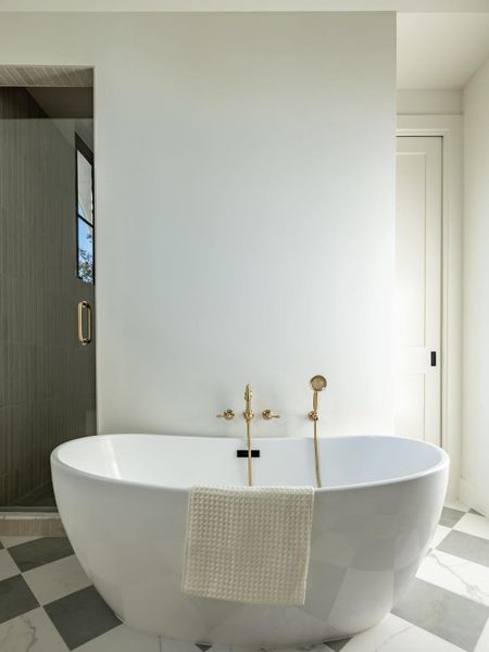 A deep soaking tub with elegant gold fixtures anchors this pristine bathroom.