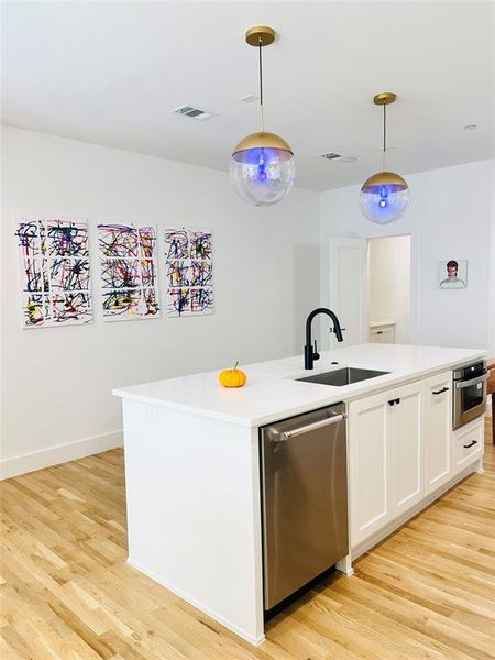 Kitchen featuring white cabinetry, pendant lighting, a center island with sink, stainless steel appliances, and light wood-type flooring Kitchen featuring white cabinetry, pendant lighting, a center island with sink, stainless steel appliances, and light wood-type flooring