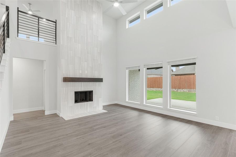 Open living room with two-story ceiling, floor-to-ceiling tiled fireplace, wood mantel, and hardwood floors