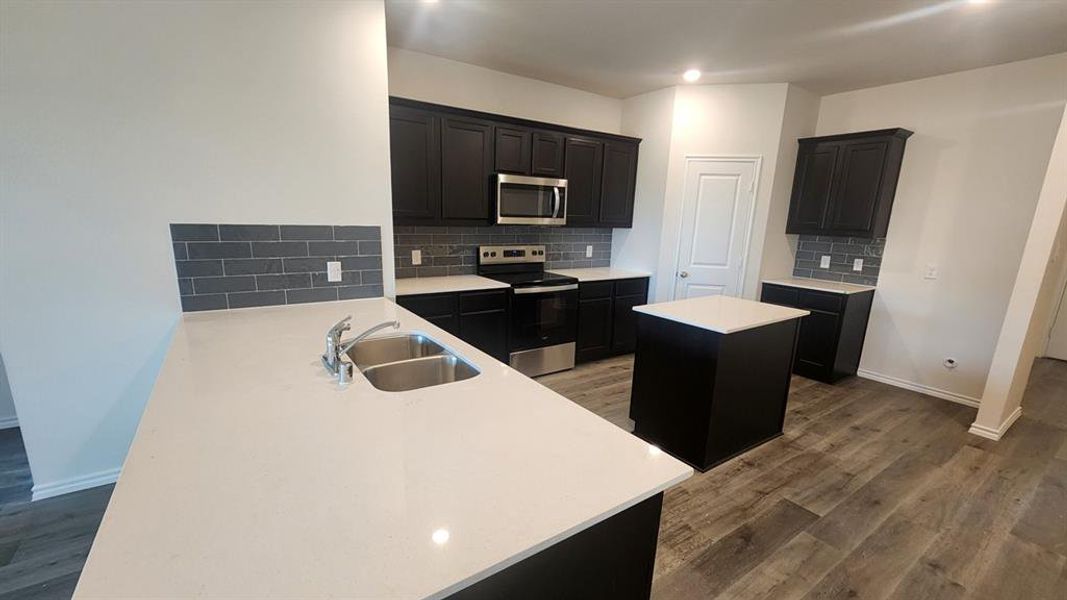 Kitchen featuring dark cabinetry, light countertops, subway tile backsplash, stainless steel appliances, and wood-finish flooring Kitchen featuring dark cabinetry, light countertops, subway tile backsplash, stainless steel appliances, and wood-finish flooring