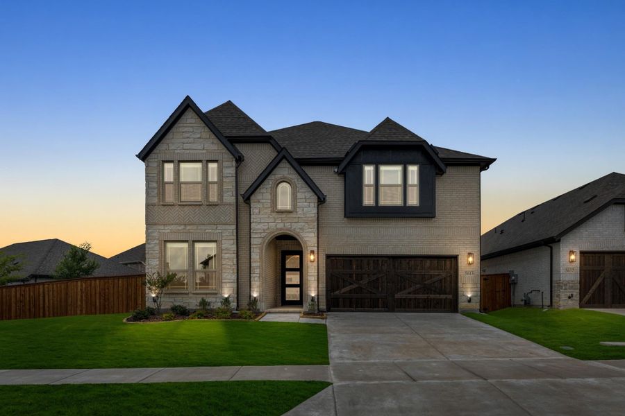 Two-story home with stone and brick exterior, two-car garage, arched entry, and green front lawn at dusk Two-story home with stone and brick exterior, two-car garage, arched entry, and green front lawn at dusk