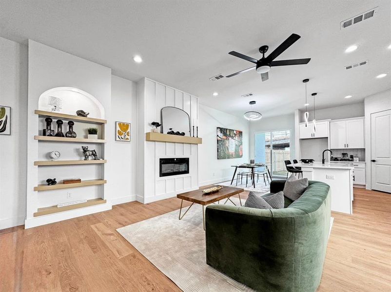 Living room with a large fireplace, ceiling fan, light wood-style flooring, recessed lighting, and built in shelves