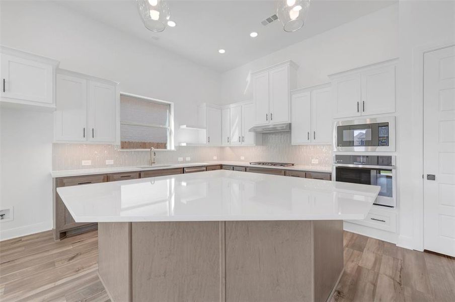 Spacious kitchen featuring a large central island with a light-toned countertop, white upper cabinetry, and contrasting darker base cabinetry Spacious kitchen featuring a large central island with a light-toned countertop, white upper cabinetry, and contrasting darker base cabinetry