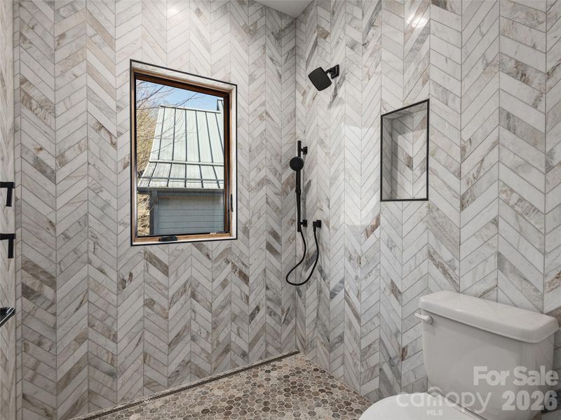 Primary ensuite bath with fully tiled walk-in shower, designer fixtures, window for natural light, and detailed tilework extending from floor to ceiling.