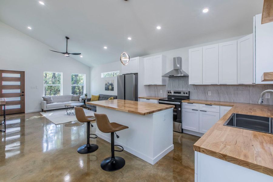 Kitchen featuring wood counters, backsplash, a breakfast bar area, white cabinetry, and high vaulted ceiling