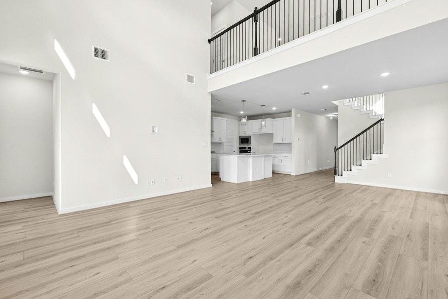 Unfurnished living room featuring light wood-style floors, stairs, and a high ceiling