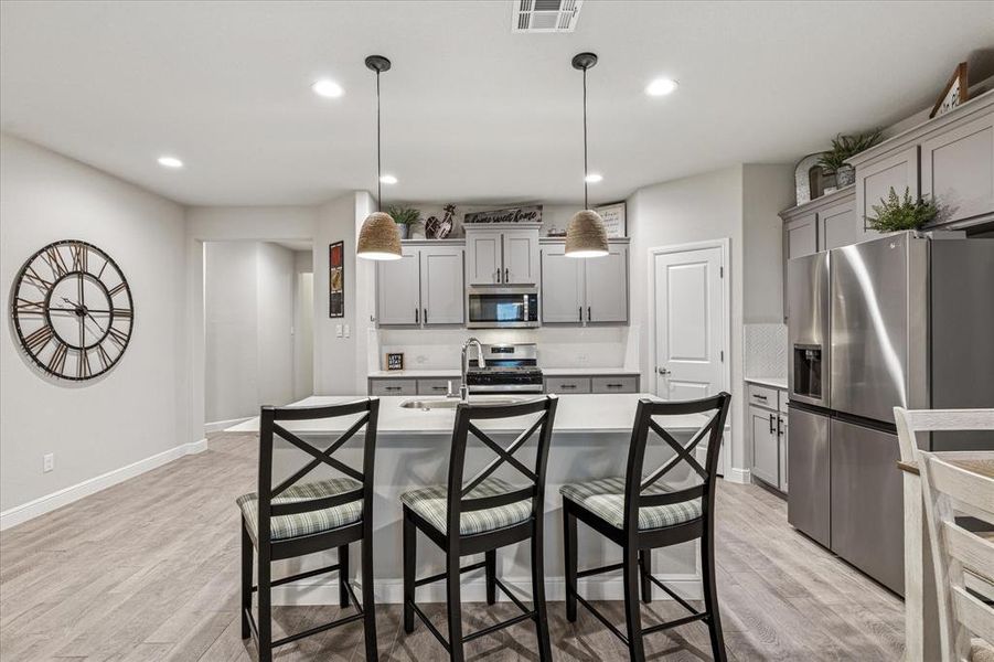 Kitchen with appliances with stainless steel finishes, gray cabinets, light countertops, a kitchen bar, and light wood-style flooring Kitchen with appliances with stainless steel finishes, gray cabinets, light countertops, a kitchen bar, and light wood-style flooring