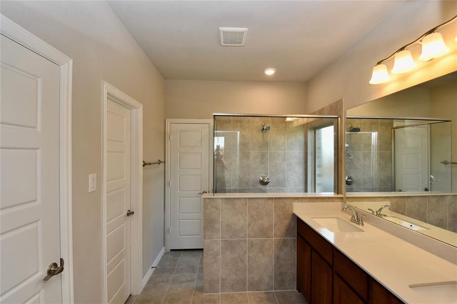 Full bath featuring tiled shower, light tile patterned flooring, double vanity, and recessed lighting