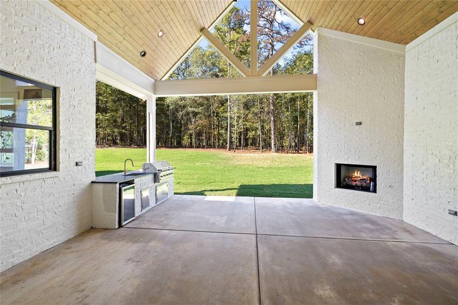 View of patio with exterior kitchen and a warm lit fireplace