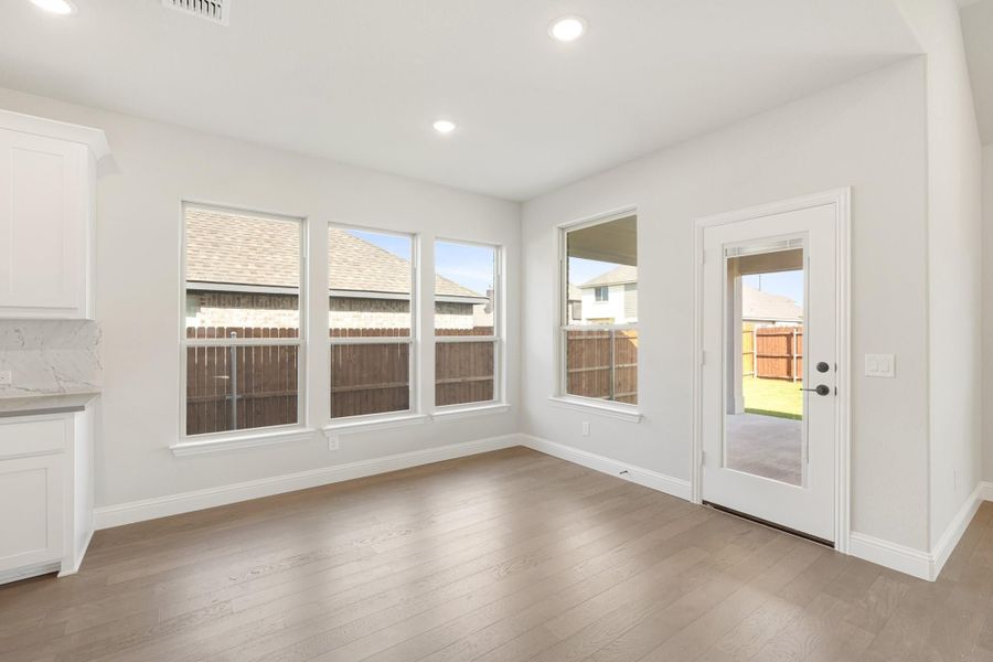Bright dining area with hardwood floors, multiple windows, and glass back door leading to fenced yard