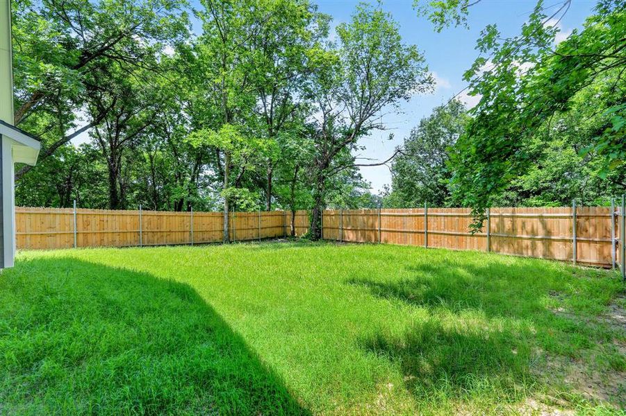 Expansive backyard with a manicured lawn, full privacy fencing, and mature perimeter trees