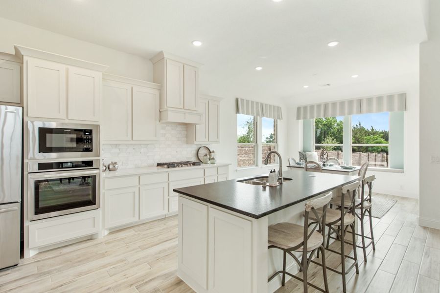 Kitchen with white cabinets, dark island with seating, stainless steel appliances, and light wood floors Kitchen with white cabinets, dark island with seating, stainless steel appliances, and light wood floors