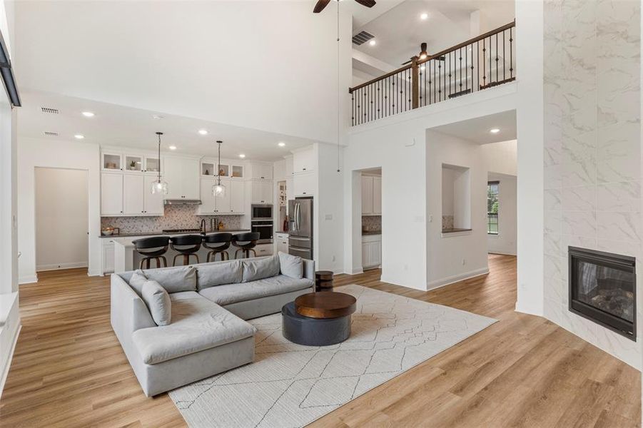 Living room featuring ceiling fan, light wood-style floors, a high ceiling, recessed lighting, and a tile fireplace Living room featuring ceiling fan, light wood-style floors, a high ceiling, recessed lighting, and a tile fireplace