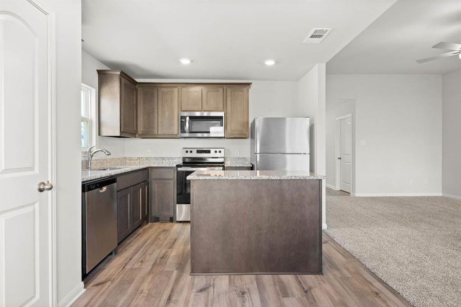 Kitchen with a center island, sink, light hardwood / wood-style flooring, ceiling fan, and appliances with stainless steel finishes