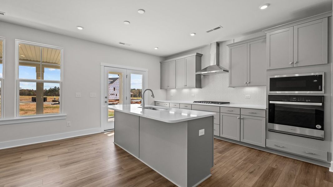 Burton Design gourmet kitchen with wall oven and microwave, vented hood, & cooktop. Lakeside Glen by DRB Homes in York, SC.