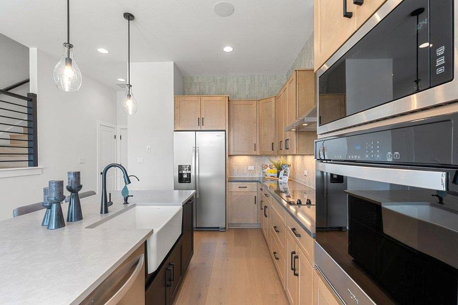 Contemporary kitchen featuring light wood-finish cabinetry, stainless steel appliances, a built-in oven and microwave, and a large island with an undermount farmhouse sink and matte black faucet