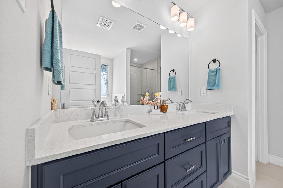 Spacious primary bathroom featuring a dual-sink vanity with premium quartz countertops, complemented by high-end cabinetry and drawers equipped with soft-close hardware for a seamless, quiet experience. The room is finished with sophisticated nickel fixtures, custom vanity lighting, and modern ceramic tile flooring, creating a clean, high-quality aesthetic that highlights the home's thoughtful updates and craftsmanship. Spacious primary bathroom featuring a dual-sink vanity with premium quartz countertops, complemented by high-end cabinetry and drawers equipped with soft-close hardware for a seamless, quiet experience. The room is finished with sophisticated nickel fixtures, custom vanity lighting, and modern ceramic tile flooring, creating a clean, high-quality aesthetic that highlights the home's thoughtful updates and craftsmanship.