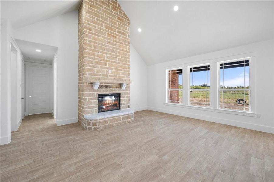 Unfurnished living room featuring light wood-type flooring, a fireplace, and high vaulted ceiling