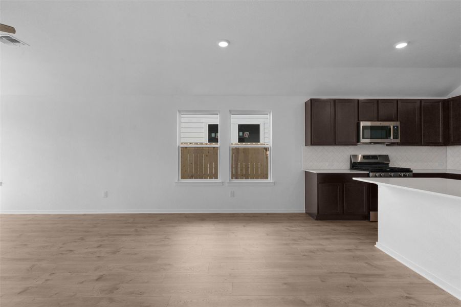 Kitchen with dark wood finish cabinetry, stainless steel appliances, light wood finished floors, tasteful backsplash, and recessed lighting