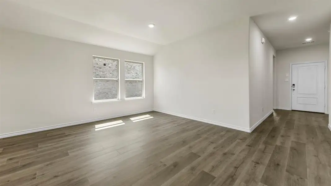 Spacious interior room featuring wood-finish flooring, recessed lighting, and white baseboards