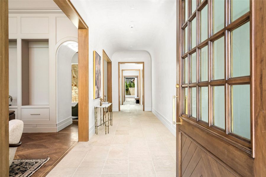 A gracious entry sets the tone with an oversized custom mahogany pivot door, timeless limestone flooring, Venetian plaster walls, and a barrel-vaulted ceiling. White oak cased openings create a beautifully framed progression through the home, offering a glimpse of the private courtyard beyond. A gracious entry sets the tone with an oversized custom mahogany pivot door, timeless limestone flooring, Venetian plaster walls, and a barrel-vaulted ceiling. White oak cased openings create a beautifully framed progression through the home, offering a glimpse of the private courtyard beyond.
