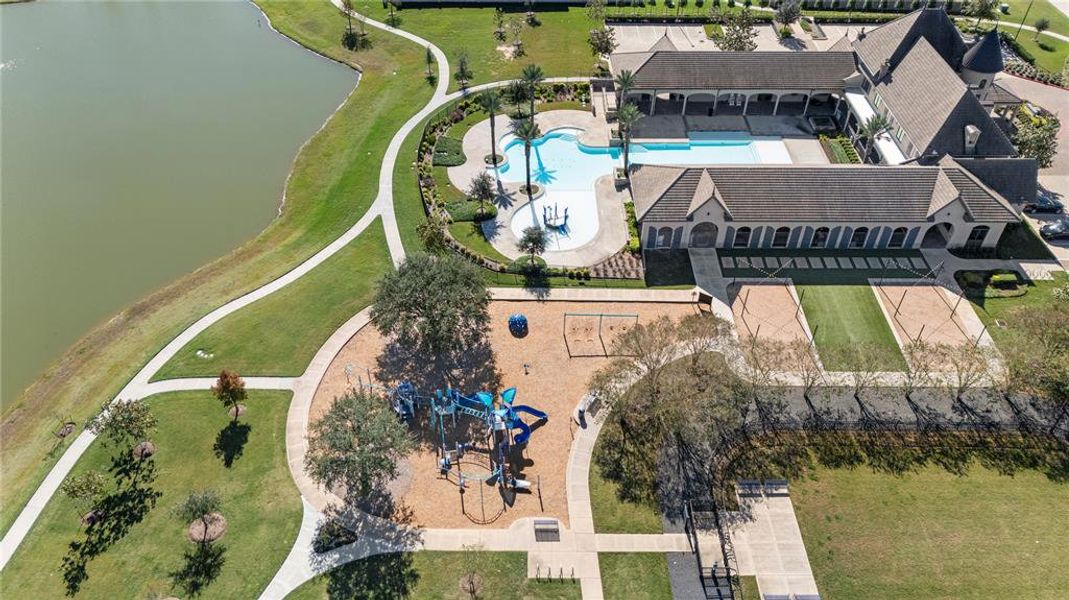 This is an aerial view of the expansive outdoor pool area, adjacent to the serene lake. The property includes a playground and well-manicured lawns, offering a blend of sophistication and recreational amenities.