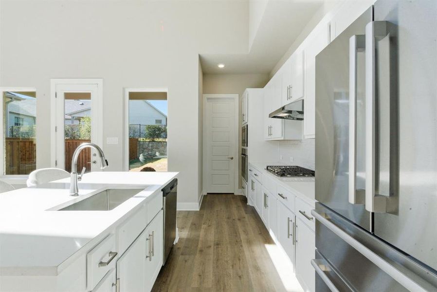 Kitchen with stainless steel appliances, white cabinetry, a center island with sink, light wood finished floors, and decorative backsplash