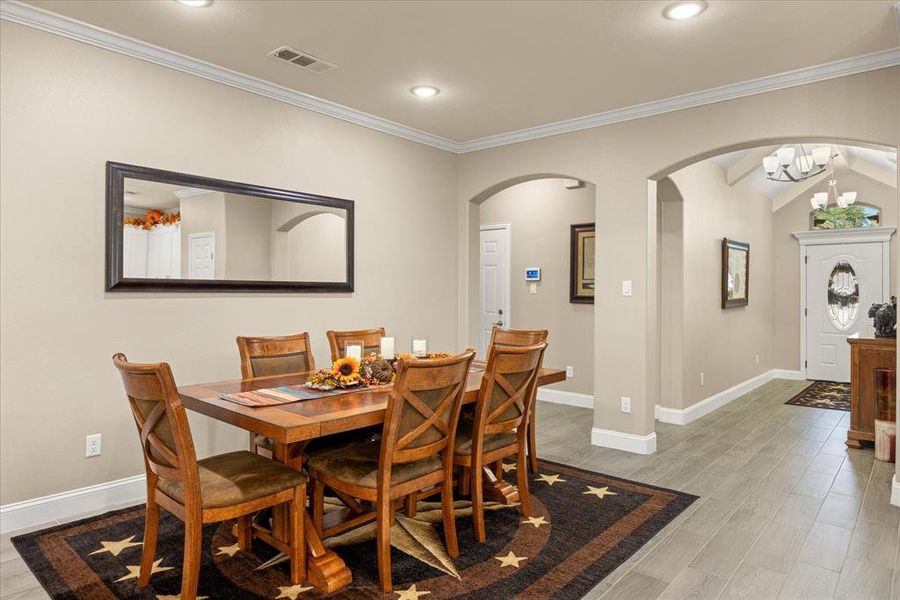 Dining room featuring arched walkways, light wood-type flooring, crown molding, vaulted ceiling, and a chandelier Dining room featuring arched walkways, light wood-type flooring, crown molding, vaulted ceiling, and a chandelier