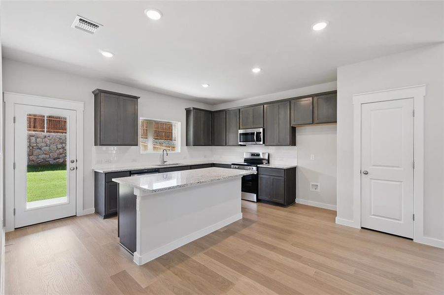 Kitchen with stainless steel appliances, a kitchen island, light stone countertops, light wood-style floors, and recessed lighting