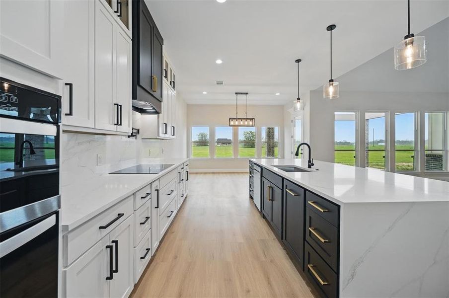 Kitchen featuring white cabinets, hanging light fixtures, stainless steel double oven, dark cabinetry, and light stone countertops Kitchen featuring white cabinets, hanging light fixtures, stainless steel double oven, dark cabinetry, and light stone countertops