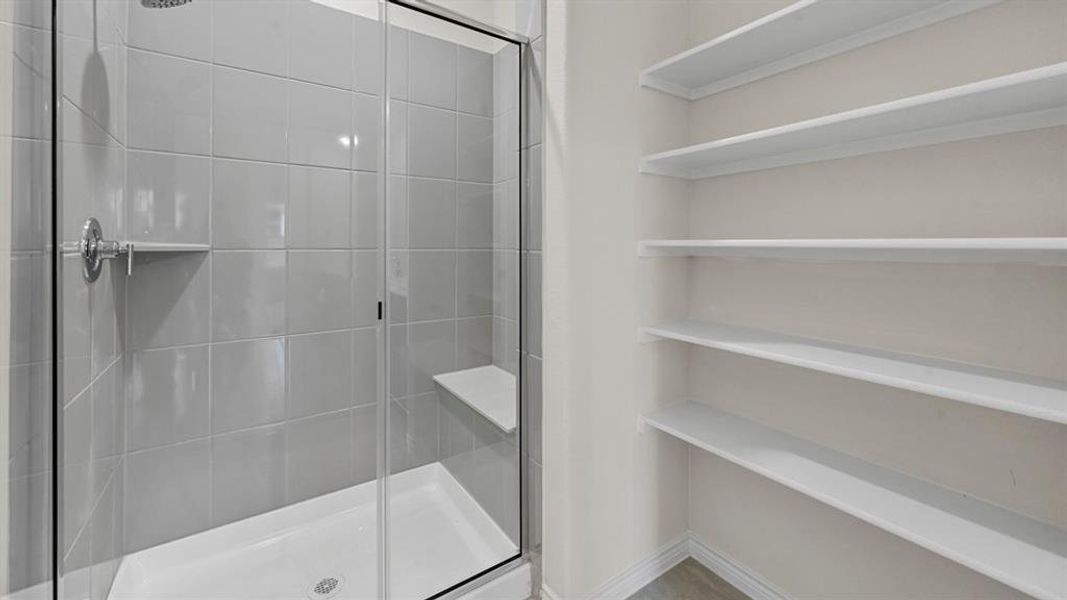Shower with clear glass enclosure and light gray tile surround, featuring a built-in bench and recessed shelving