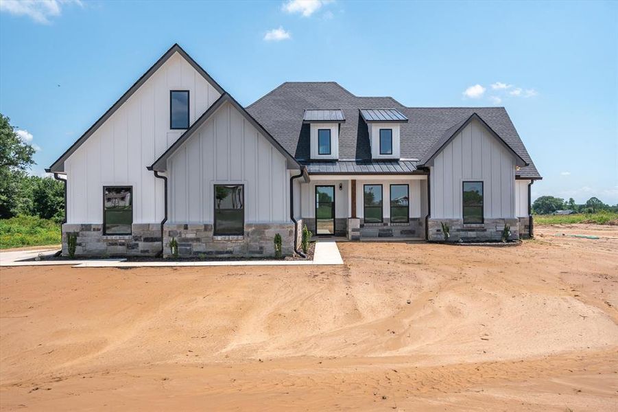 Modern farmhouse style home featuring board and batten siding, stone siding, roof with shingles, and a standing seam roof