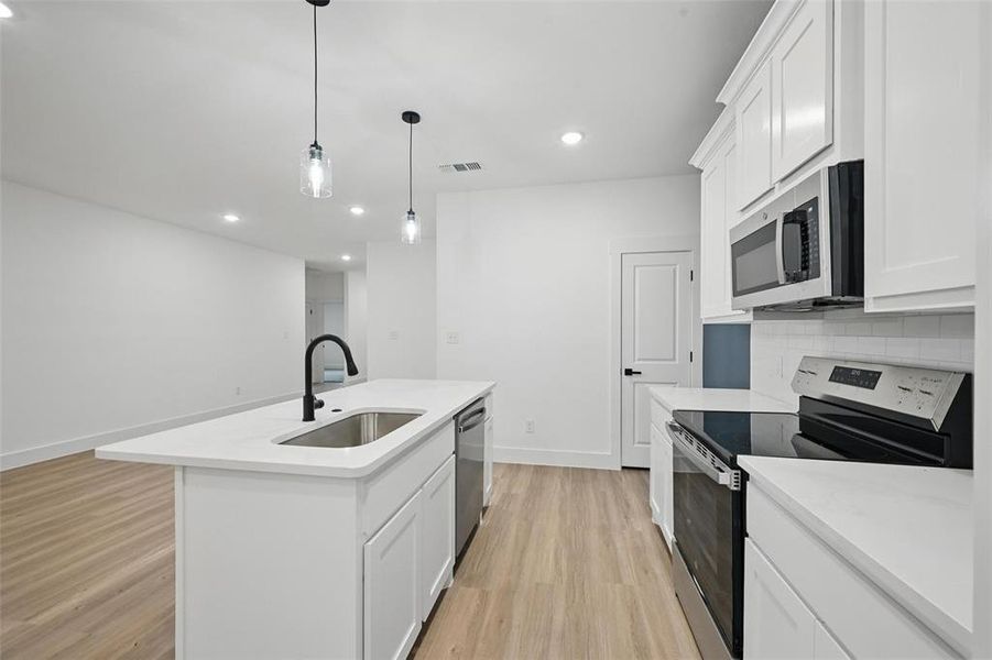 Kitchen featuring stainless steel appliances, a sink, light wood-style flooring, backsplash, and light countertops