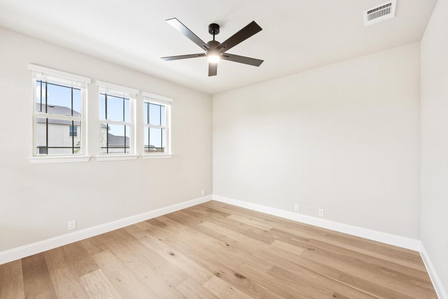 Empty bedroom with light hardwood floors, ceiling fan, and two white-framed windows