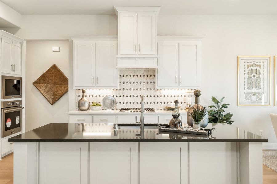 Kitchen with white cabinets, dark island countertop, patterned tile backsplash, and double wall ovens
