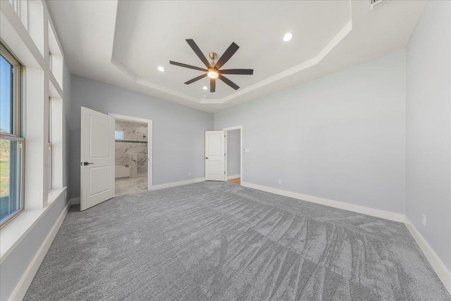Unfurnished bedroom with a tray ceiling, ceiling fan, ensuite bathroom, recessed lighting, and carpet Unfurnished bedroom with a tray ceiling, ceiling fan, ensuite bathroom, recessed lighting, and carpet